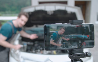 Male recording a video of him and a car on with their phone on a tripod