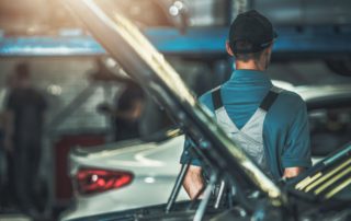 technician standing behind a car in a repair shop