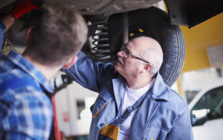 Technician and shop owner inspecting underneath a car in an automotive shop