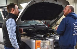 Technician and manager standing by a car talking